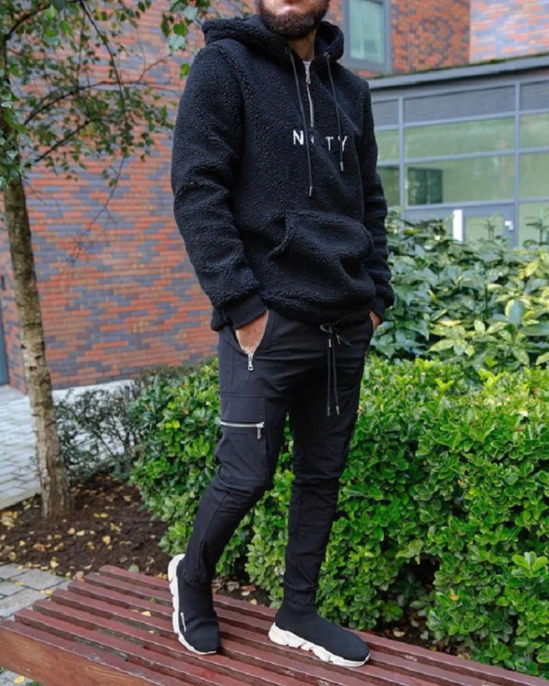 Person wearing a black tracksuit with 'Nasty' text, standing outdoors.