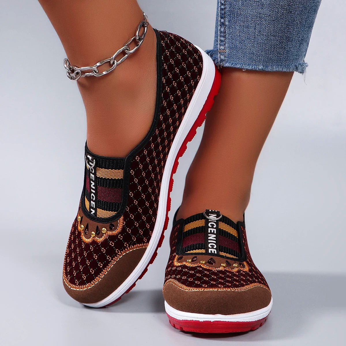 Brown patterned shoes with red soles worn by a person on a light gray background