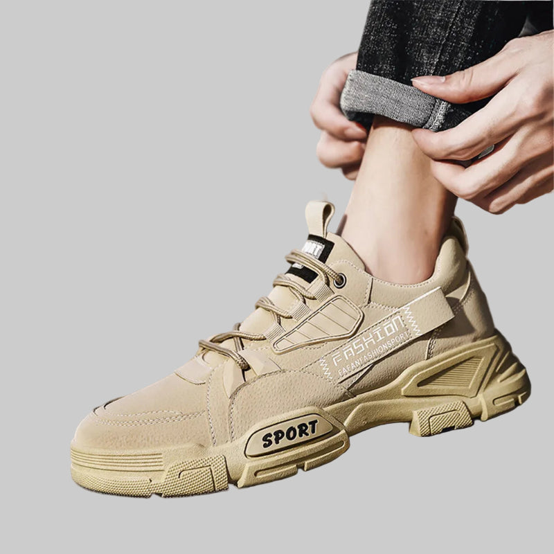 Beige sneakers with 'Fashion Sport' branding being worn by a person sitting on a stone surface.