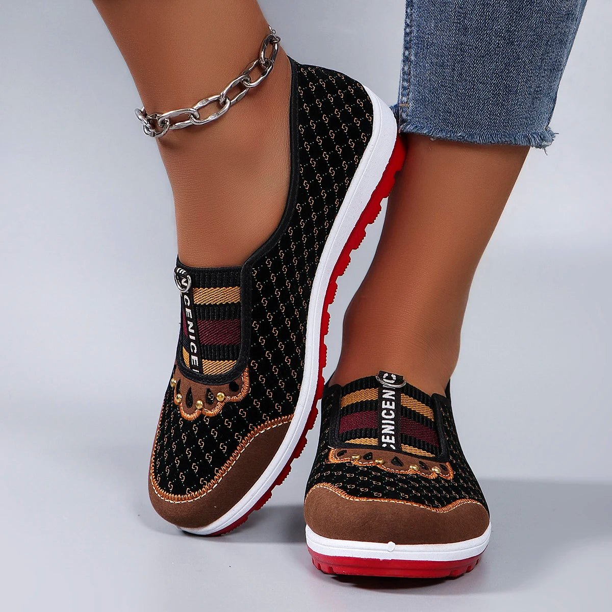Black and brown slip-on shoes with red soles worn by a person on a light gray background