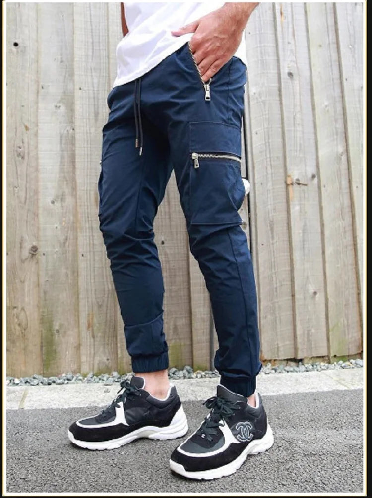 Person wearing navy jogger pants and black sneakers against a wooden fence background