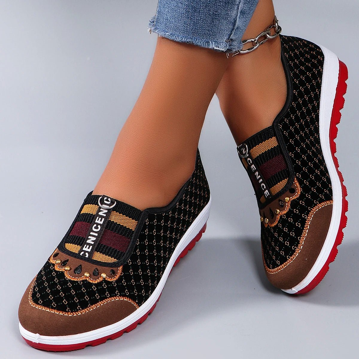 Black patterned slip-on shoes with red soles worn by a person on a gray background