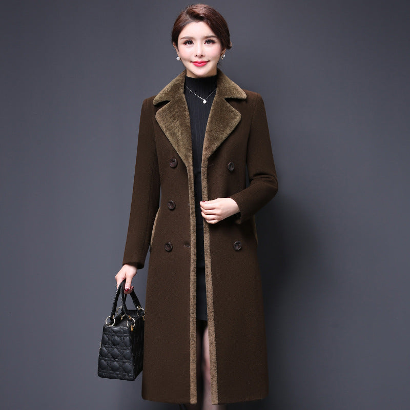 Woman wearing a brown coat holding a black handbag against a gray background