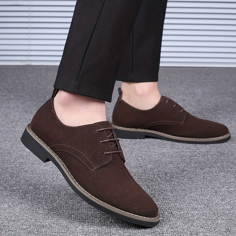 Brown suede shoes worn with black pants on a gray floor.