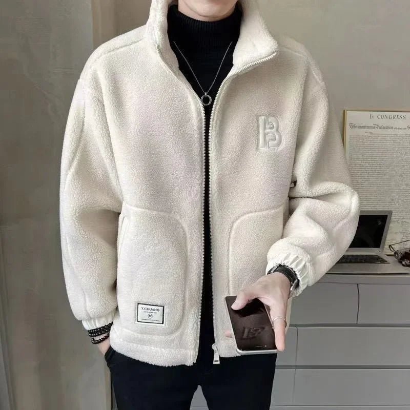 Person wearing a beige fleece jacket with a brand logo, holding a phone indoors.